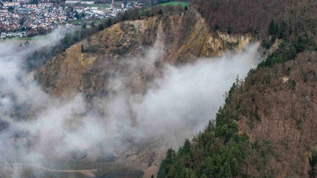 Fog rolling over a forested hillside with a town nearby.